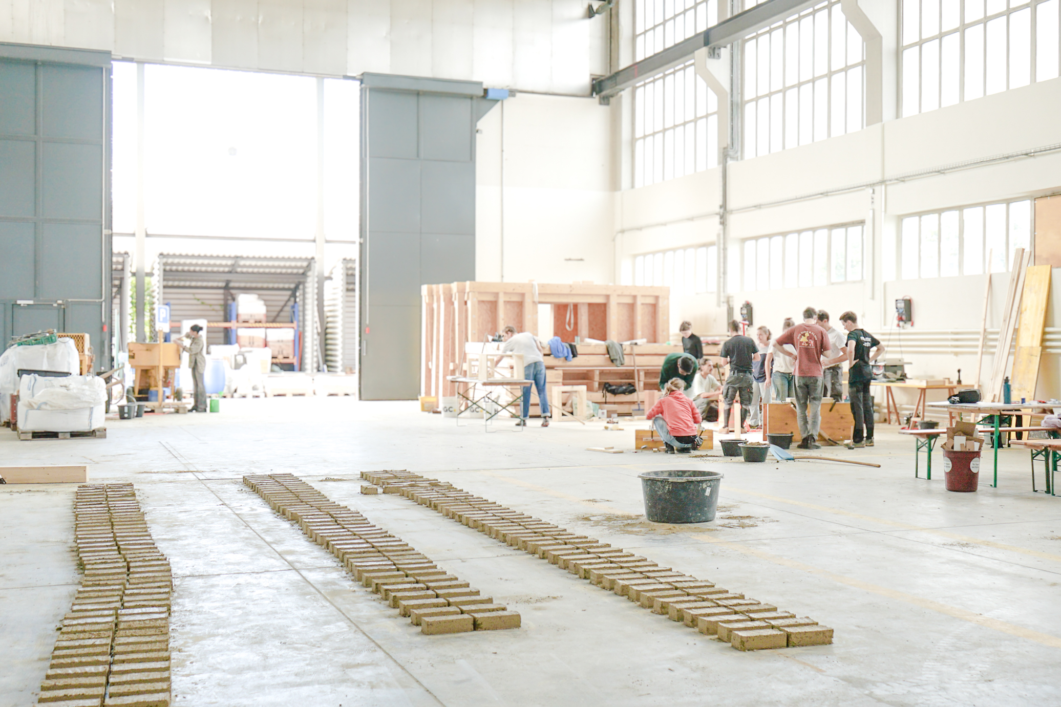 Das Bild zeigt den Lehmbau Workshop 2025 in einer Lagerhalle der Empa. Zu sehen sind Adobe-Lehmziegel und die Workshopgruppe.
